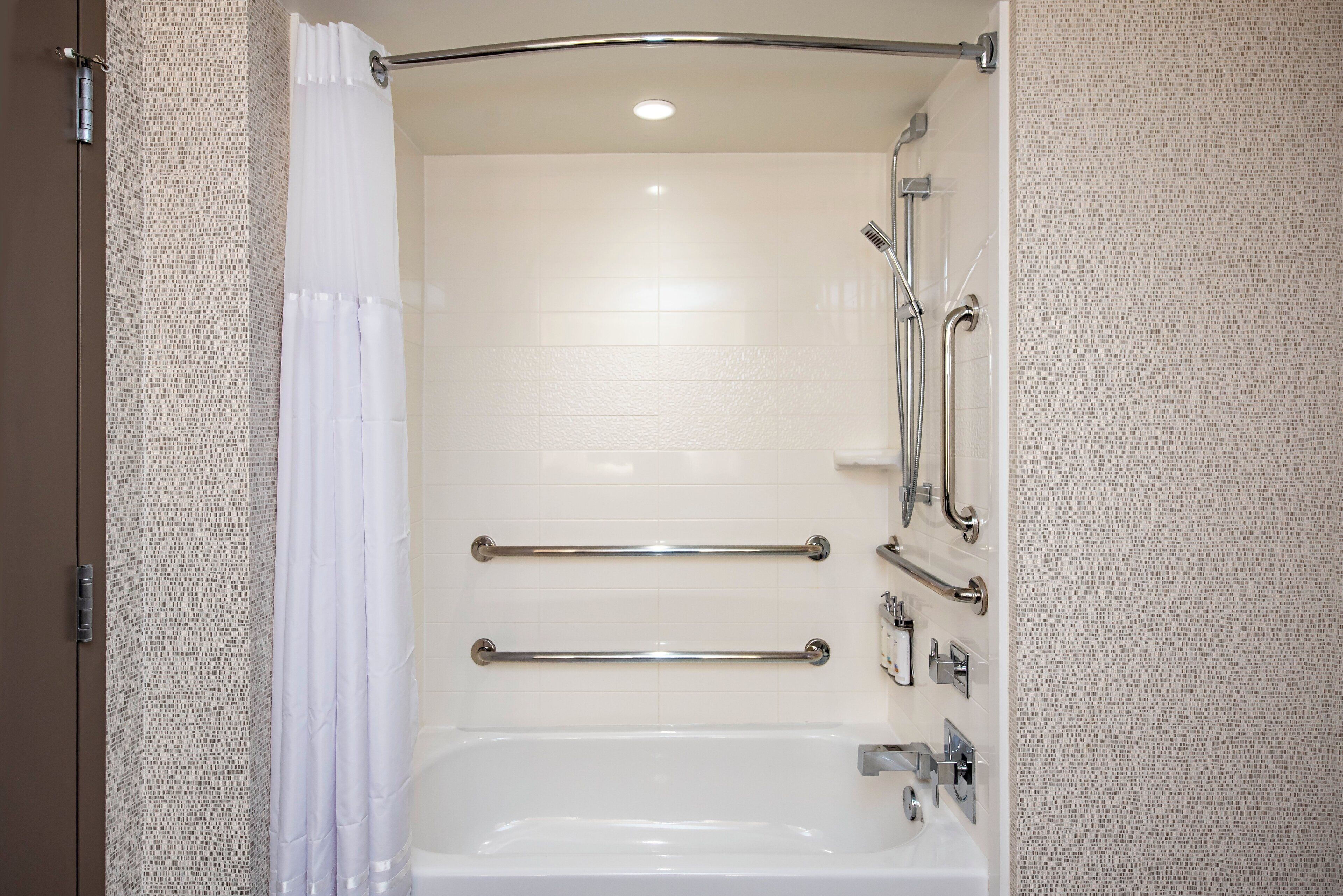 A modern bathroom with a walk-in shower, grab bars, and a white bathtub.