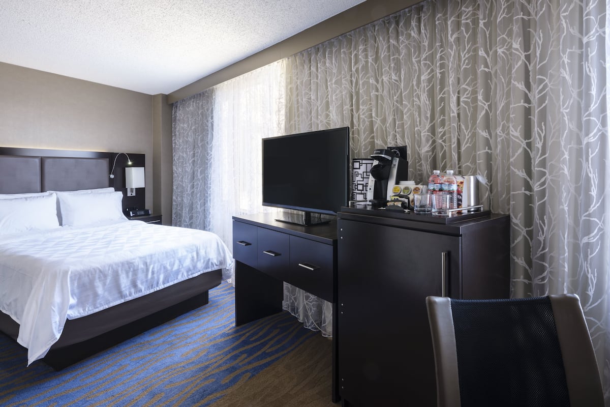 Habitación de hotel con cama, escritorio con televisor, cafetera y una silla.