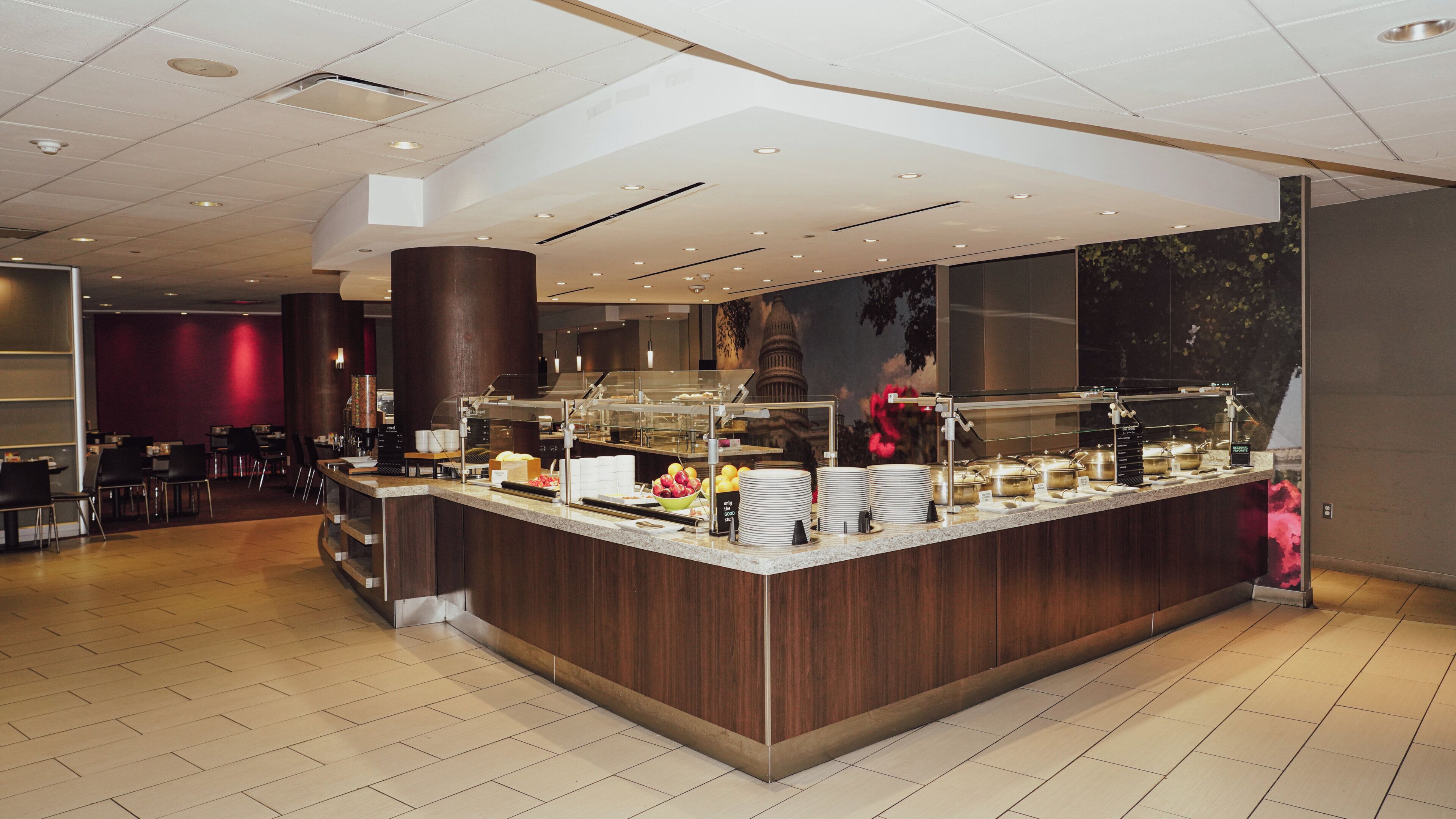 A modern breakfast bar with a variety of food items, a seating area with tables and chairs, and a large pillar in the center.