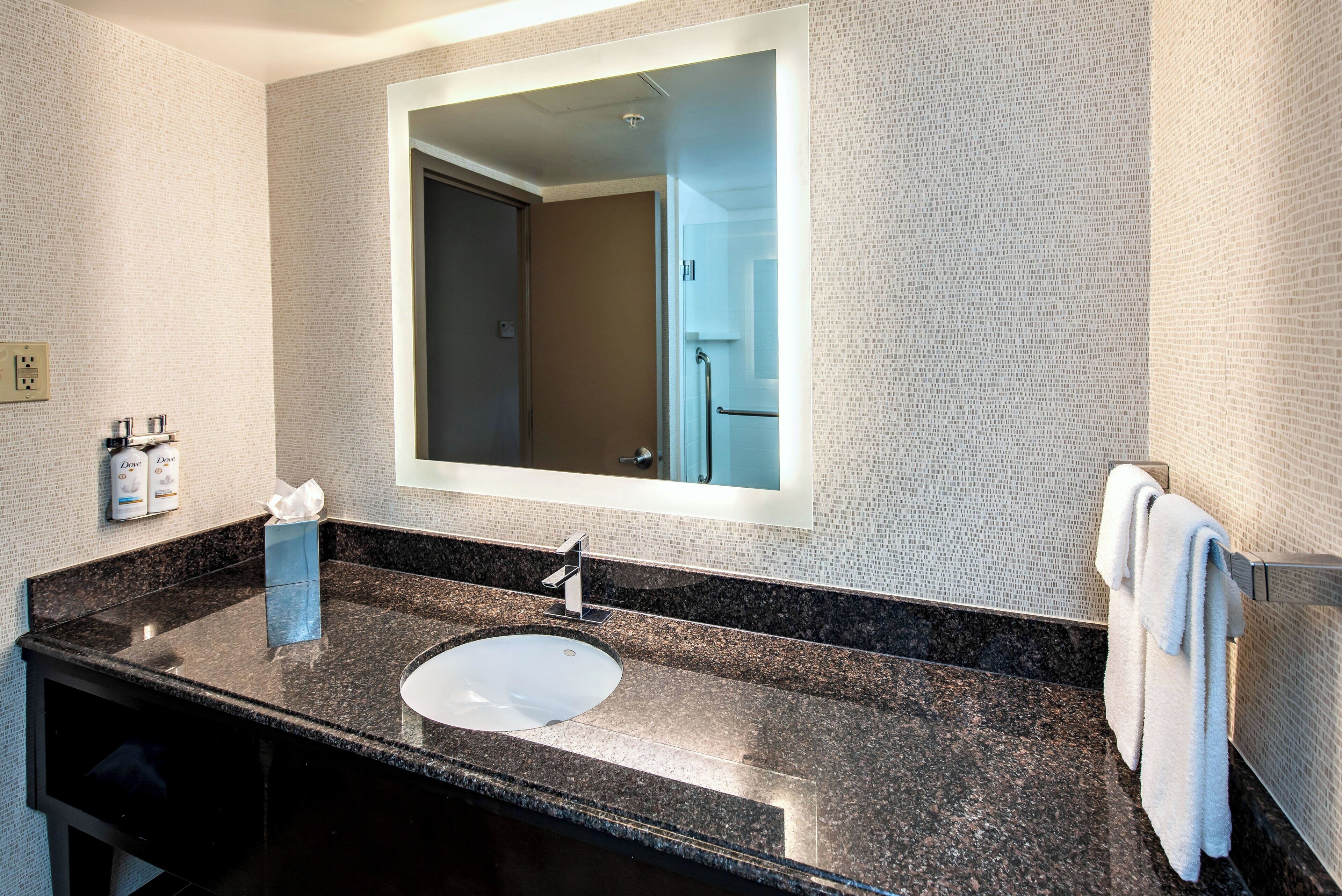 Une salle de bain moderne avec un comptoir en granit, un lavabo blanc, un grand miroir et un porte-serviettes.