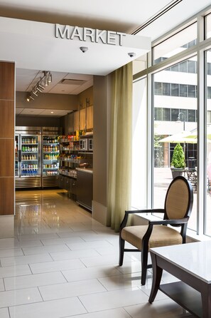 A modern interior with a 'MARKET' sign, a dining area with a table and chairs, and a kitchen area with refrigerators and shelves stocked with products.