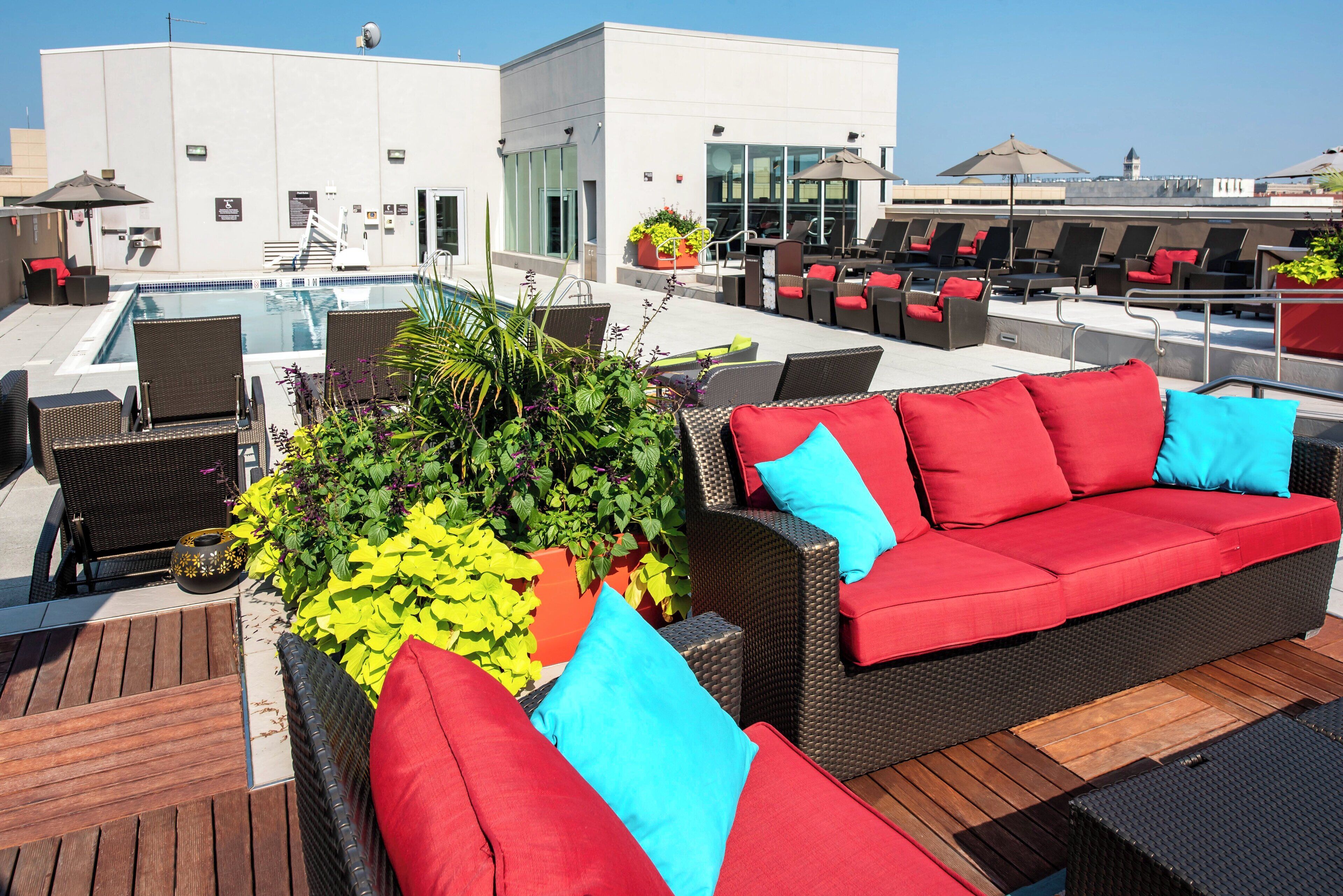 Un área de piscina en la azotea con sillones reclinables, un sofá rojo y plantas en macetas.