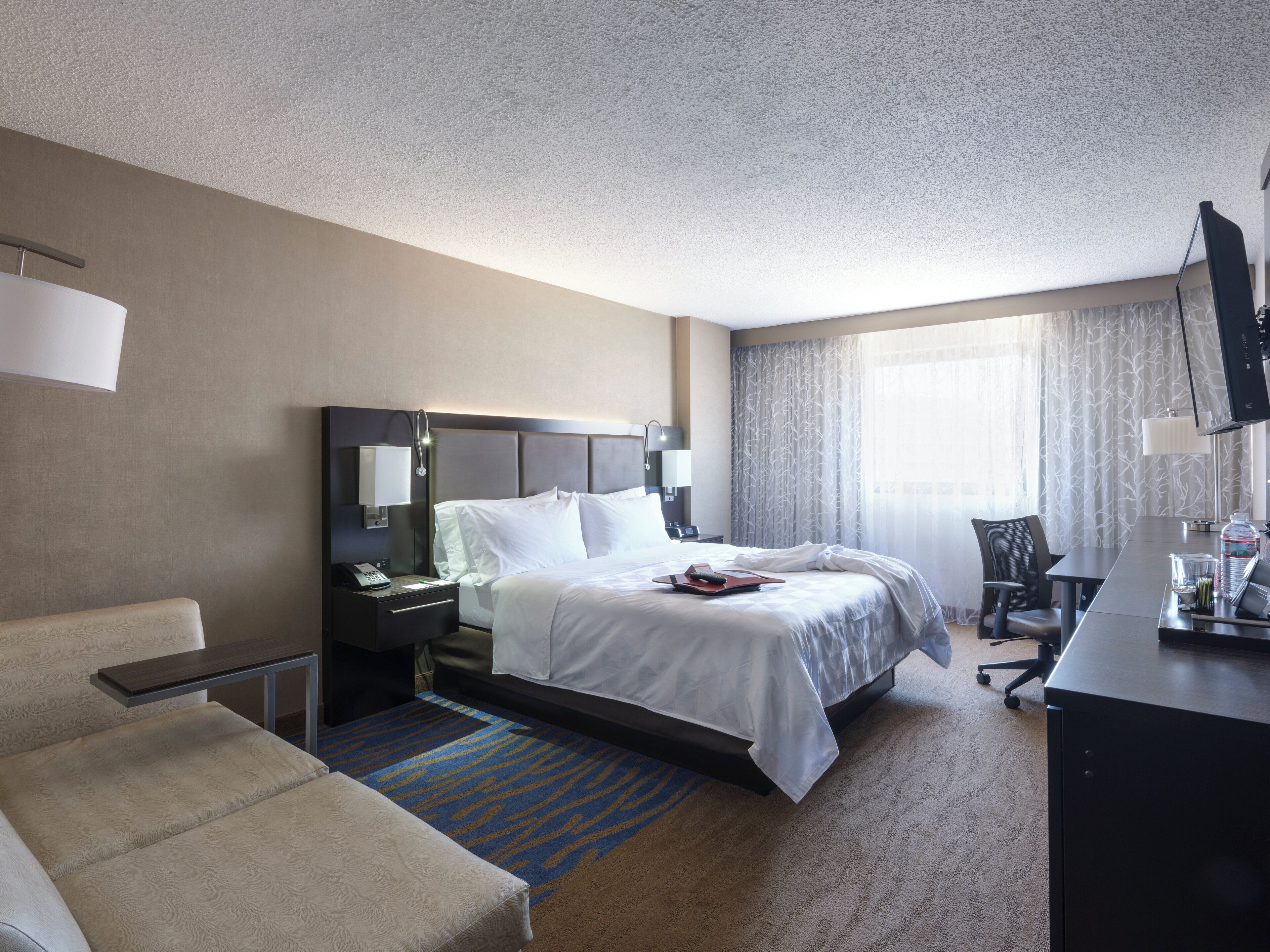 A hotel room with a bed, bedside table, lamp, chair, desk, and a television.
