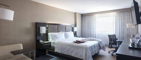 A hotel room with a bed, bedside table, lamp, chair, desk, and a television.