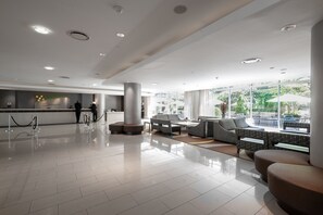 A modern lobby with a reception desk, seating area, and large windows offering a view of the outdoors.