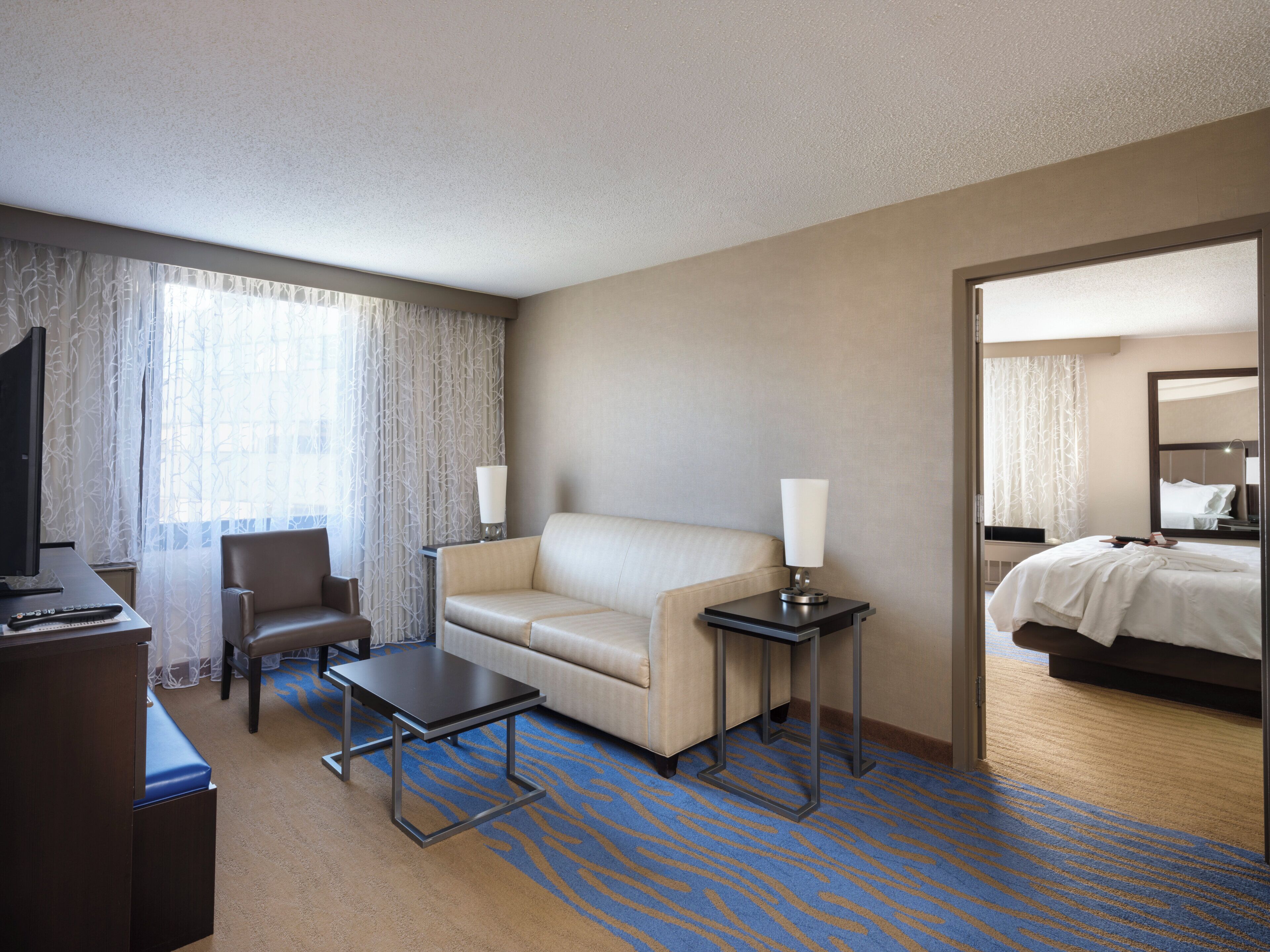 Habitación de hotel con cama, sofá, escritorio, silla, televisor y lámpara.