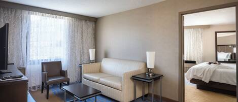 Habitación de hotel con cama, sofá, escritorio, silla, televisor y lámpara.