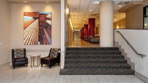 A hotel lobby with a staircase, two armchairs, a small table, and a large artwork on the wall. - Holiday Inn Washington Capitol - Natl Mall by IHG (Washington)