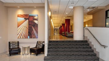 Un vestíbulo de hotel con una escalera, dos sillones, una mesita y una obra de arte grande en la pared.