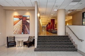 A hotel lobby with a staircase, two armchairs, a small table, and a large artwork on the wall.
