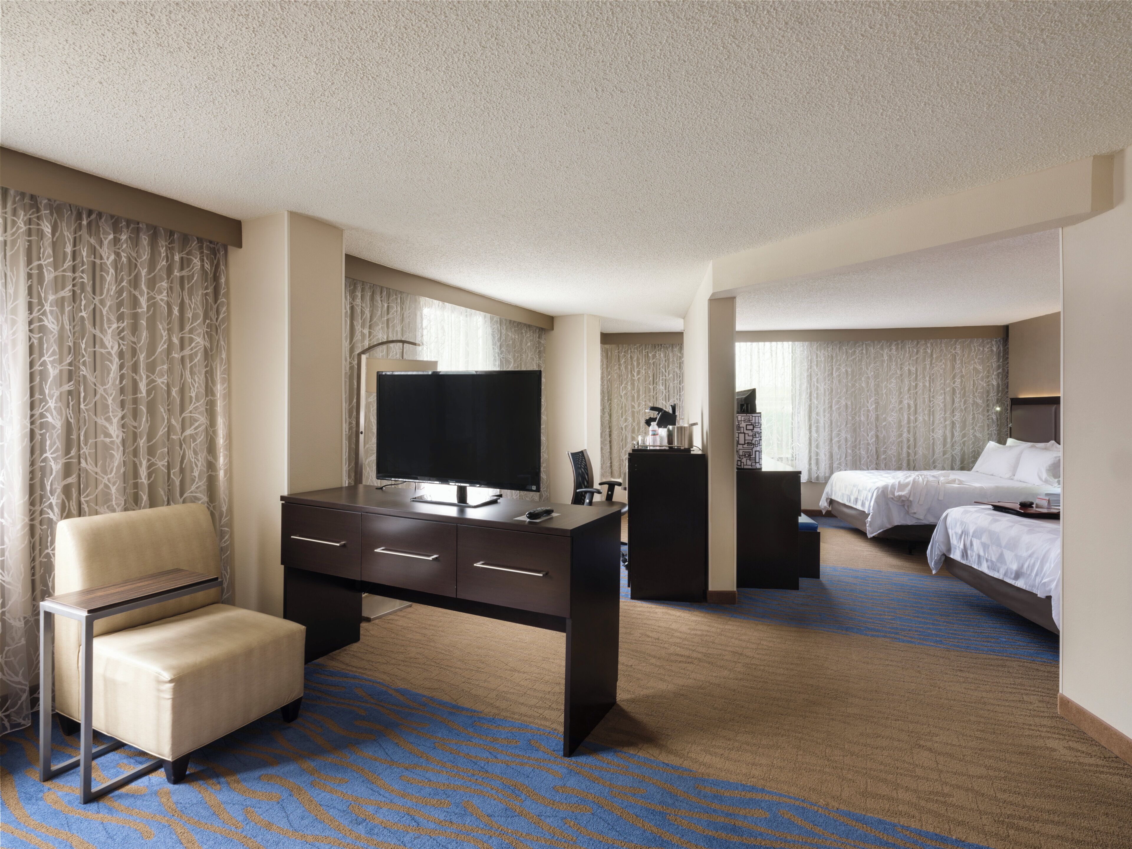A hotel room with a desk, a chair, a bed, and a television.