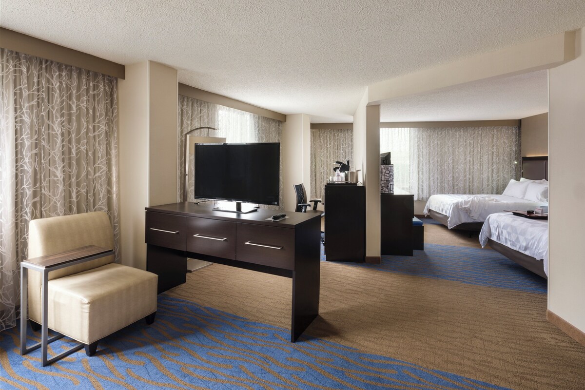 A hotel room with a desk, a chair, a bed, and a television.
