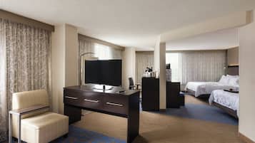 A hotel room with a desk, a chair, a bed, and a television.