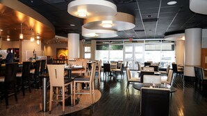 Un restaurant moderne avec un intérieur élégant, caractérisé par de hauts plafonds, un éclairage suspendu et un mélange de banquettes et de tables.