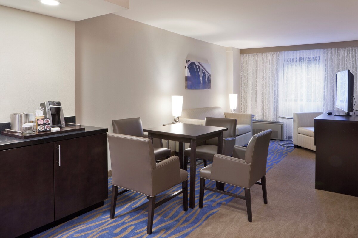 A hotel room with a dining area, a sofa, a TV, and a coffee maker.