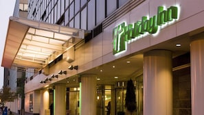 A hotel entrance with a prominent green sign, large columns, and a covered walkway.