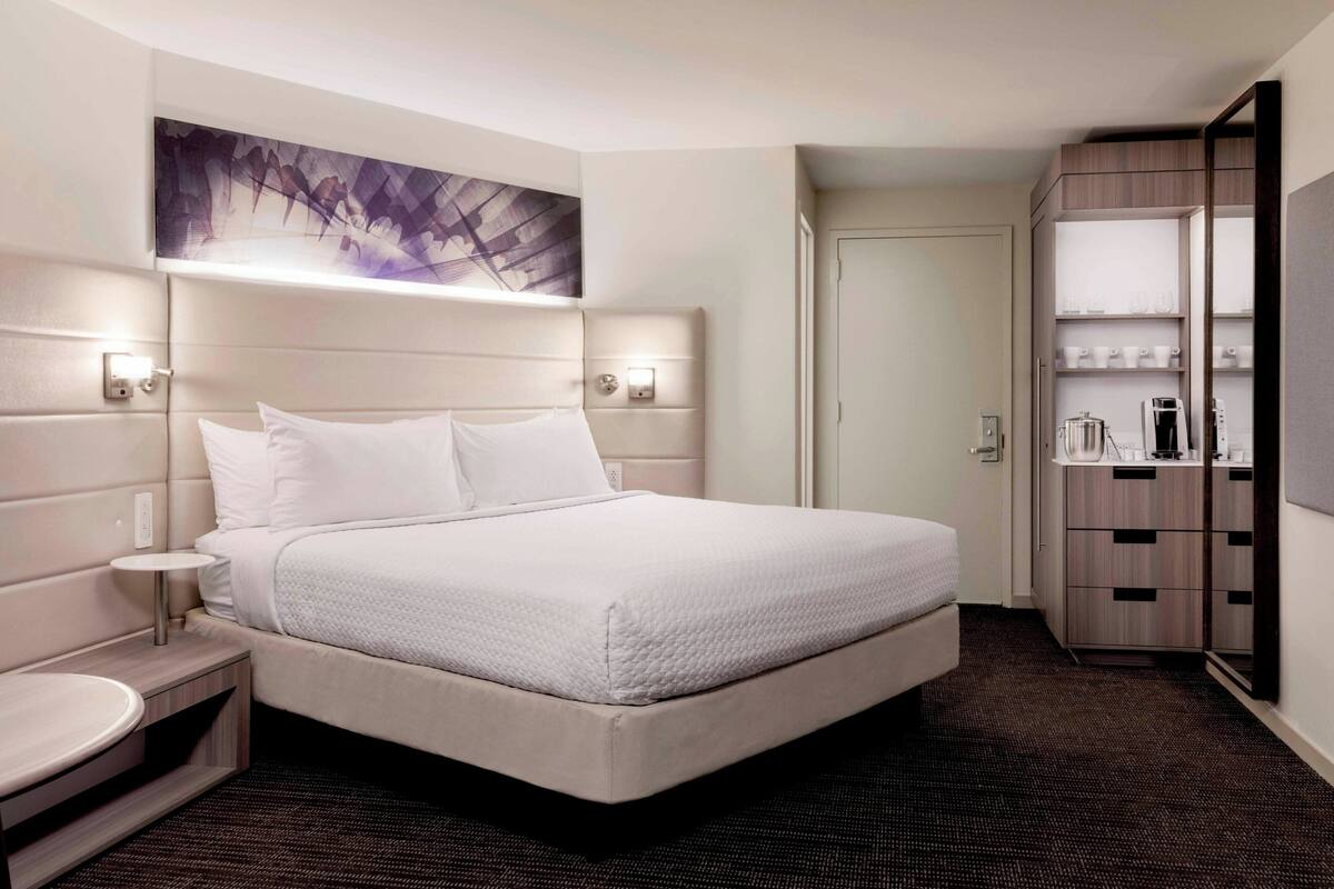 Una habitación de hotel con una cama grande, mesitas de noche, un armario y una obra de arte colgada en la pared.