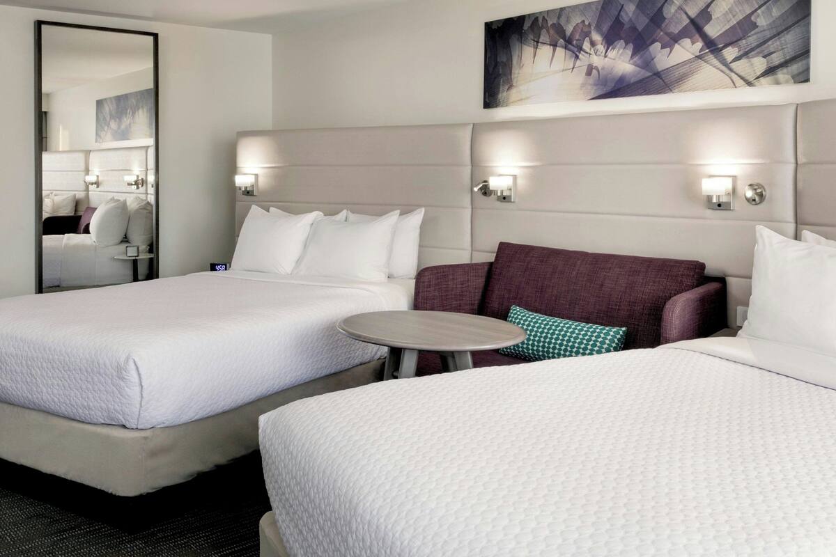 Habitación de hotel con dos camas, una mesa redonda y un espejo.