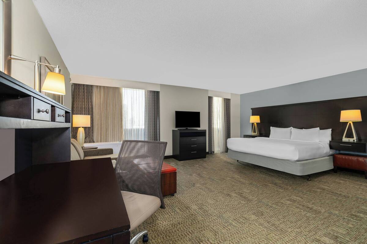 Habitación de hotel con cama, escritorio, silla, televisión y lámparas.