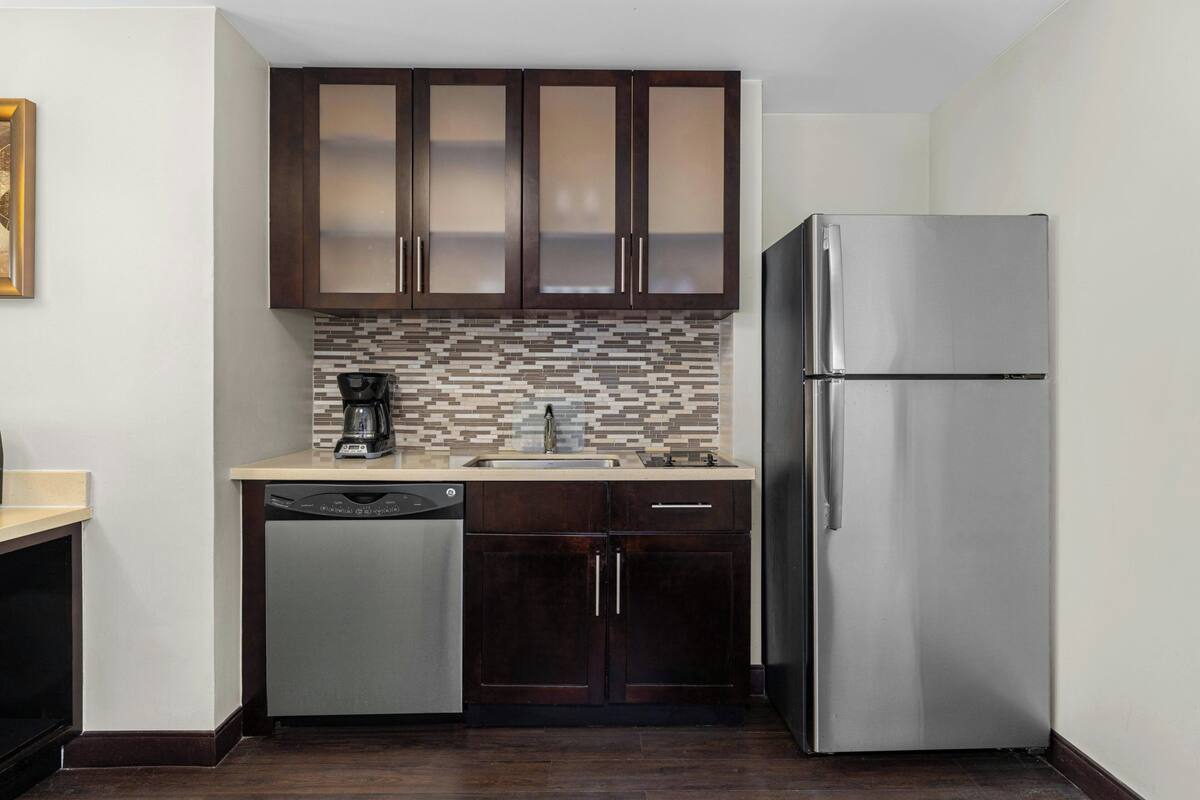 Una cocina compacta con armarios oscuros, un refrigerador de acero inoxidable, un lavavajillas y un salpicadero de azulejos.
