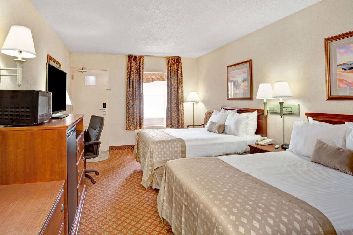 Quarto de hotel com duas camas, uma mesa com televisão, uma cadeira, abajur e telefone.
