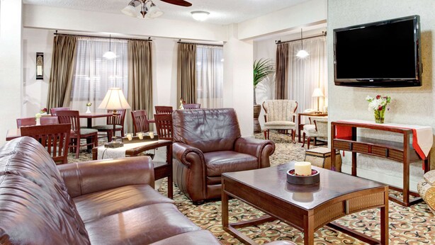 A living room with leather sofas, a wooden coffee table, a TV mounted on the wall, and a patterned carpet. - Ramada by Wyndham West Memphis (West Memphis)