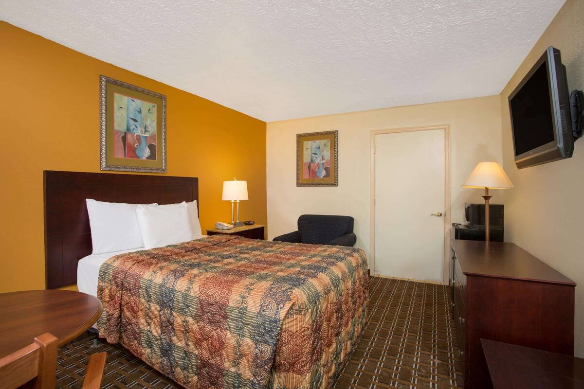 A hotel room with a bed, a desk, a chair, two lamps, and a television on the wall.
