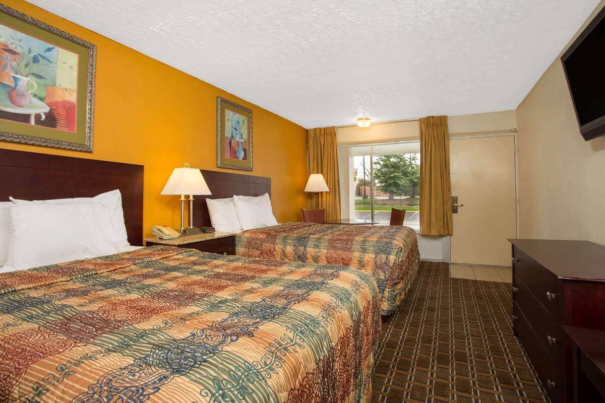 A hotel room with two beds, a nightstand, a dresser, and a television.