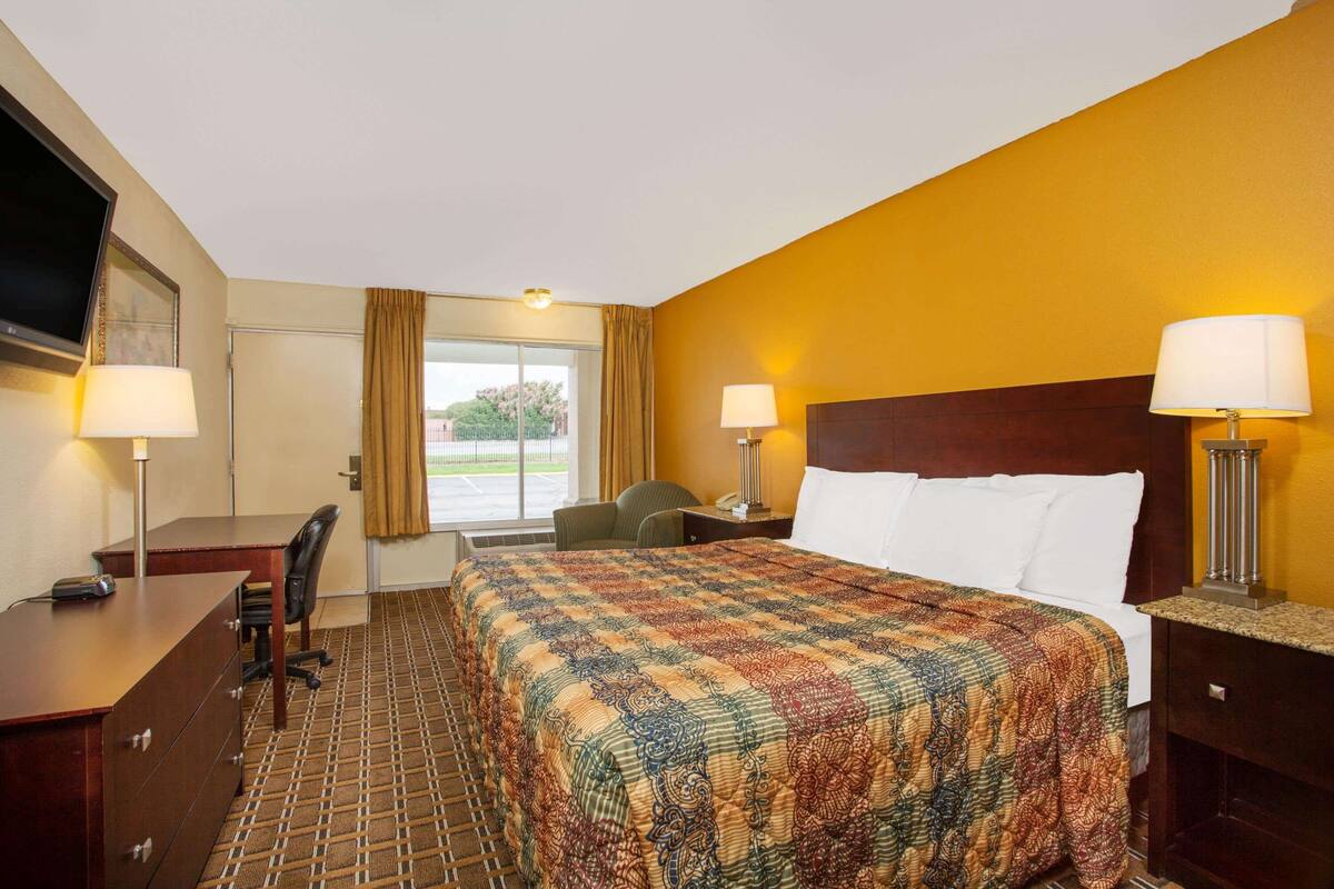 A hotel room with a large bed, a desk, a chair, and a TV.