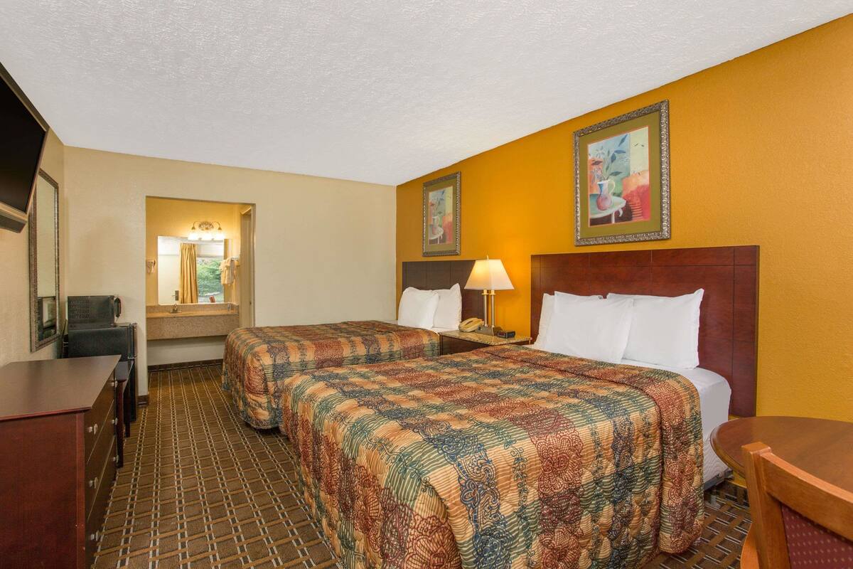 A hotel room with two beds, a desk, a chair, a lamp, and a painting on the wall.