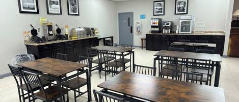 A dining area with tables and chairs, a coffee machine, and a refrigerator.
