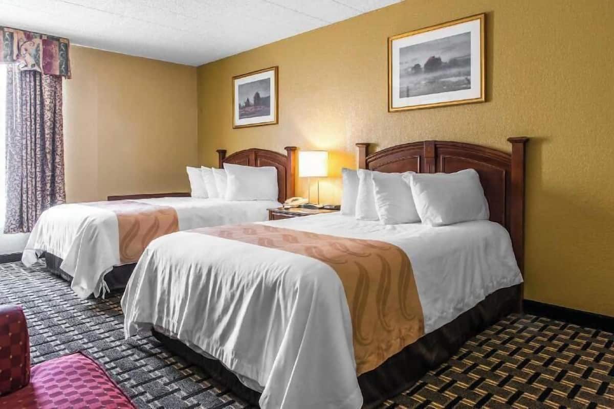 A hotel room with two beds, a nightstand, a lamp, and two framed pictures on the wall.