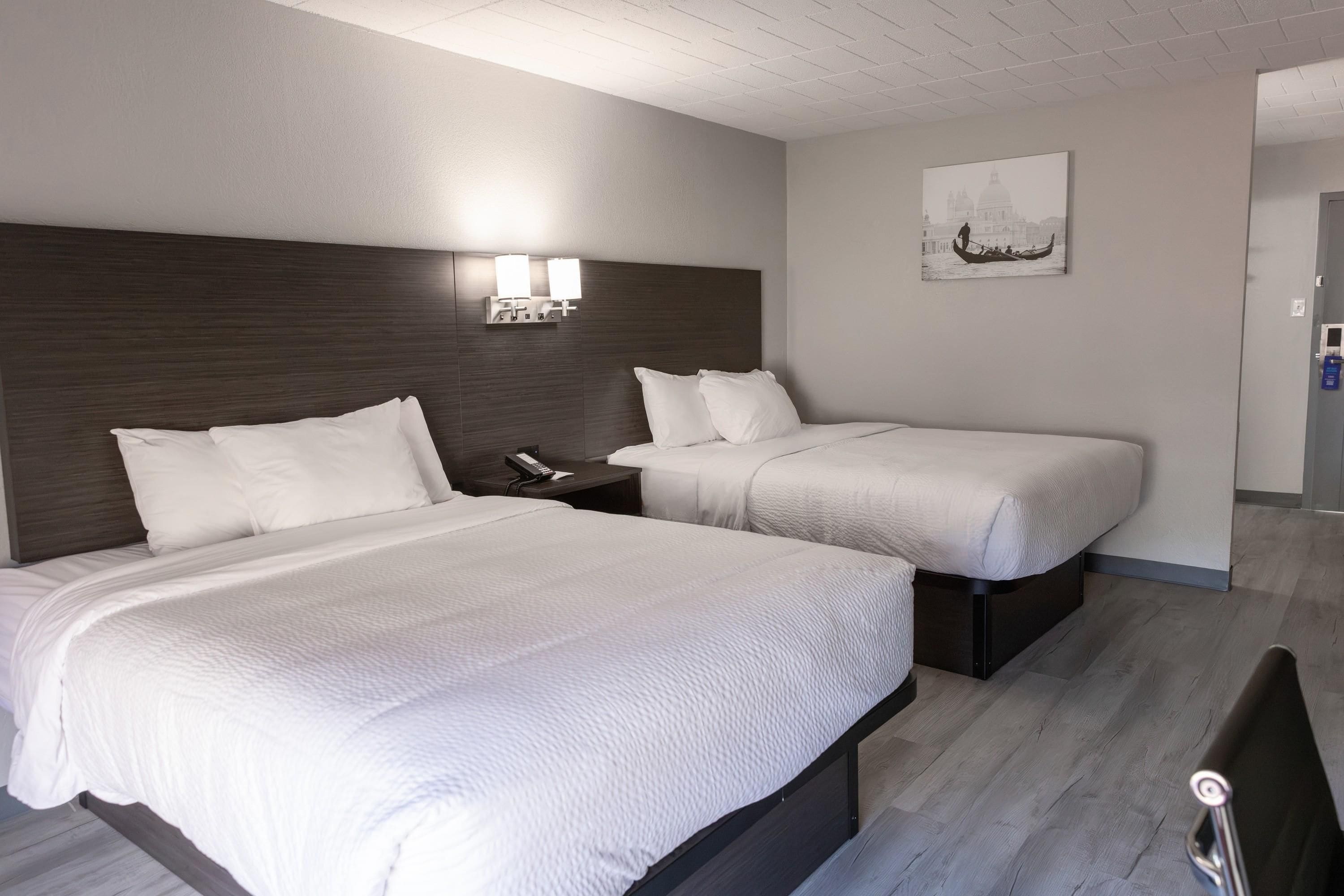 Habitación de hotel con dos camas, una mesita de noche con teléfono, una lámpara de pared e imagen enmarco.