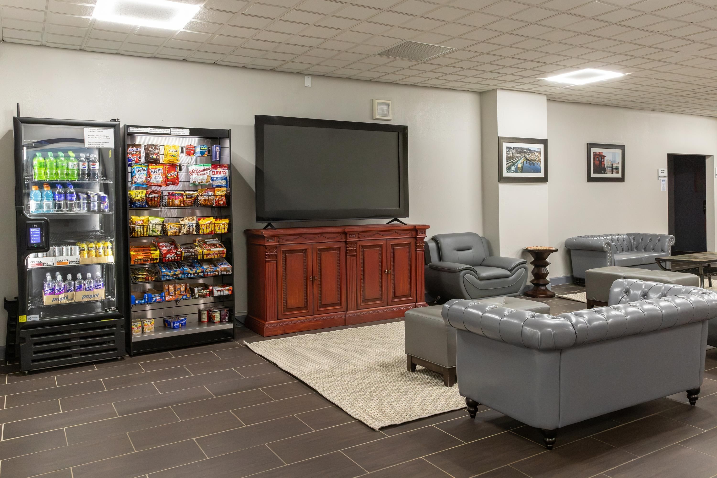 A room with a flat-screen TV, a vending machine, a sofa, and a chair.