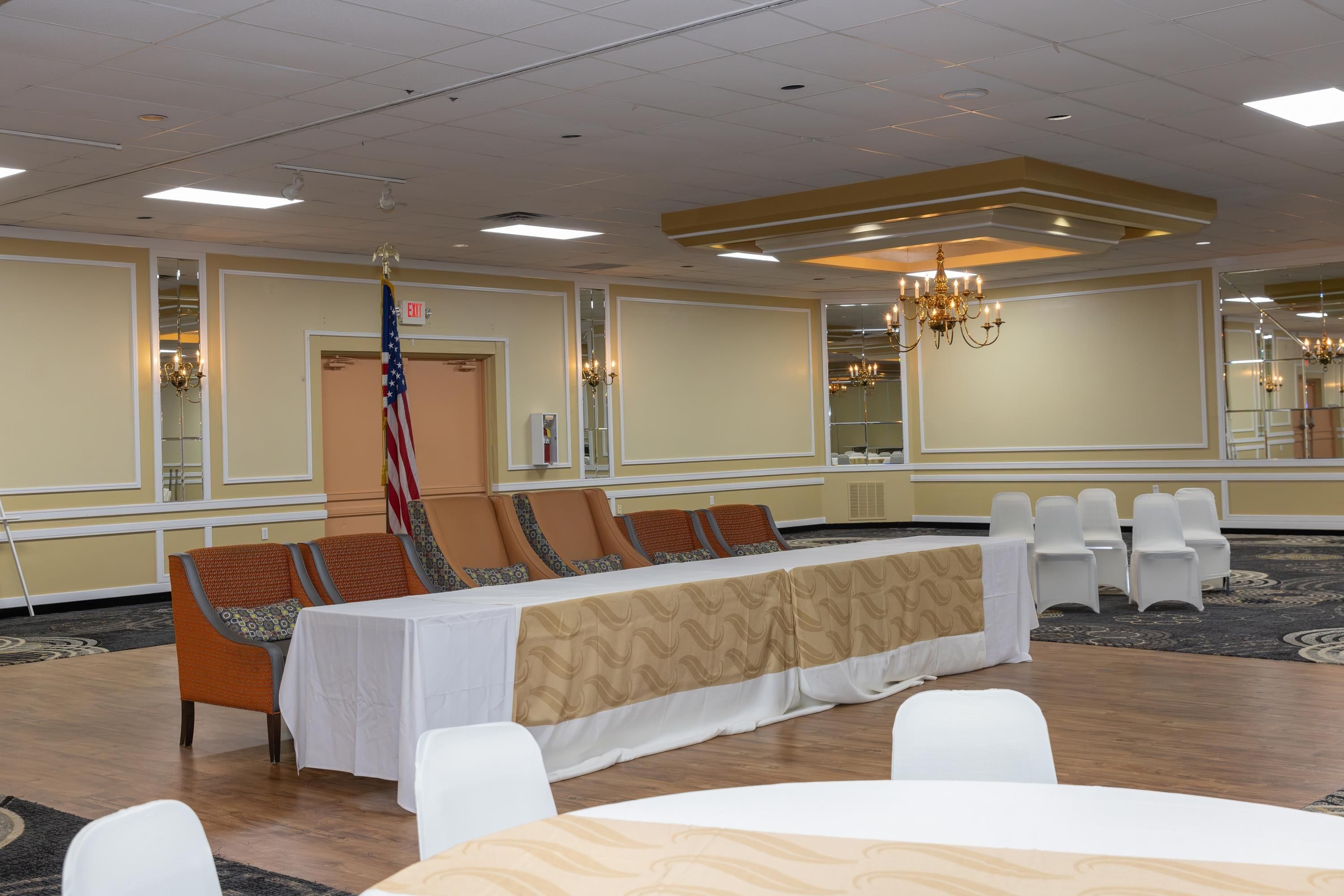 A conference room with a long table, white chairs, a chandelier, and an American flag.