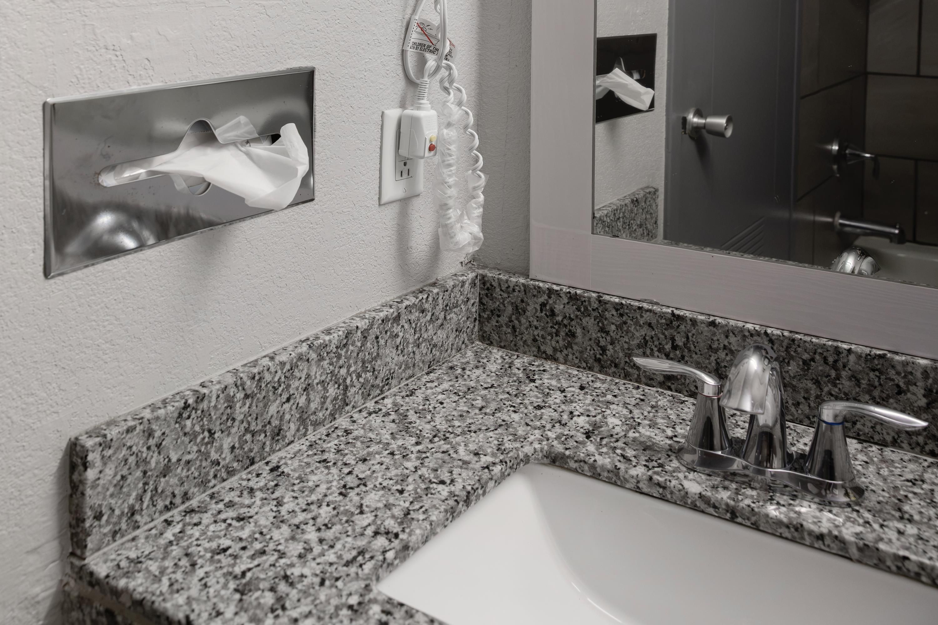 Un baño con encimera de granito, un lavabo blanco, un espejo y un secador de manos.