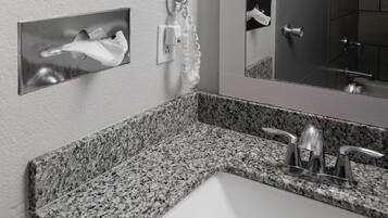 Un baño con encimera de granito, un lavabo blanco, un espejo y un secador de manos.