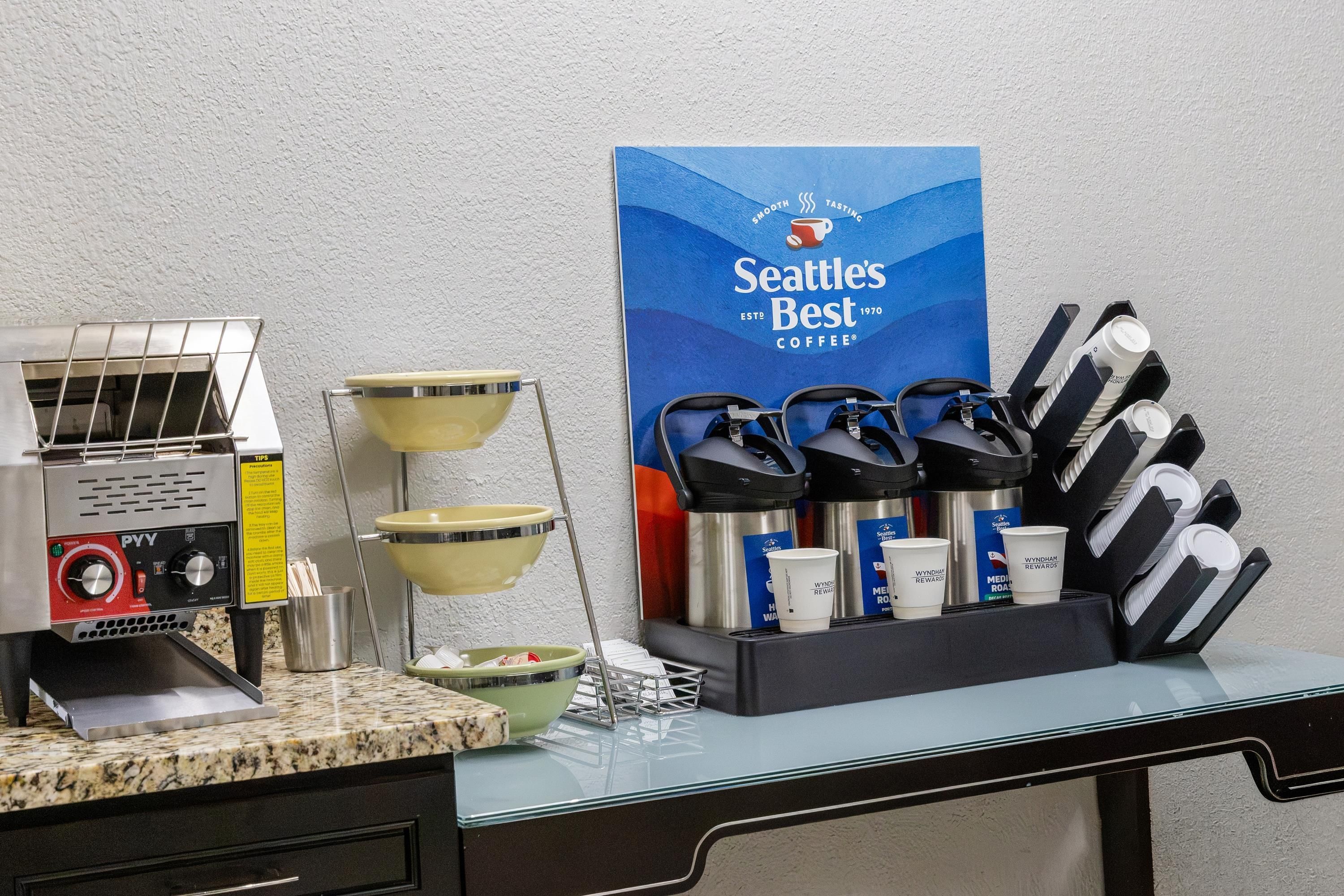 Una estación de café con un letrero de Seattle's Best Coffee, una máquina de café, vasos desechables y una bandeja con vasos y tapas.