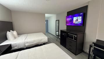 Habitación de hotel con dos camas, televisor montado en la pared, un espejo, escritorio y una kitchenette pequeña.