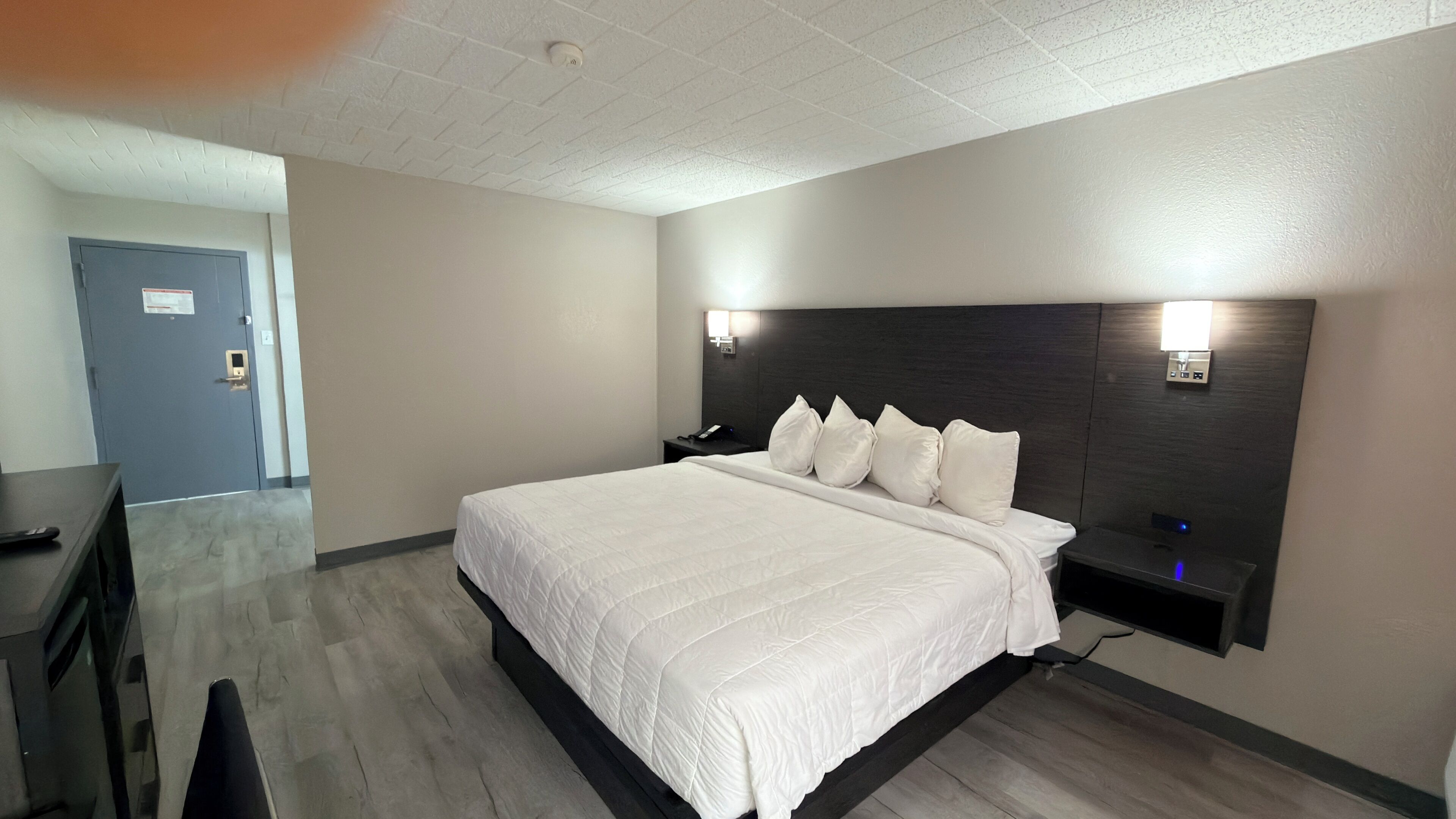 A hotel room with a large bed, bedside tables, a desk, and a door.