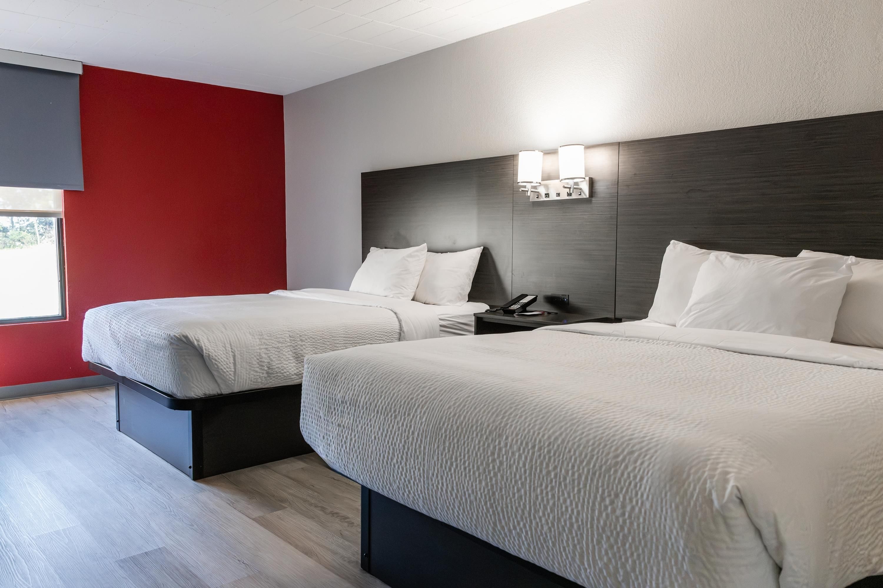 Habitación de hotel con dos camas, una pared de acento roja y un ventanal.