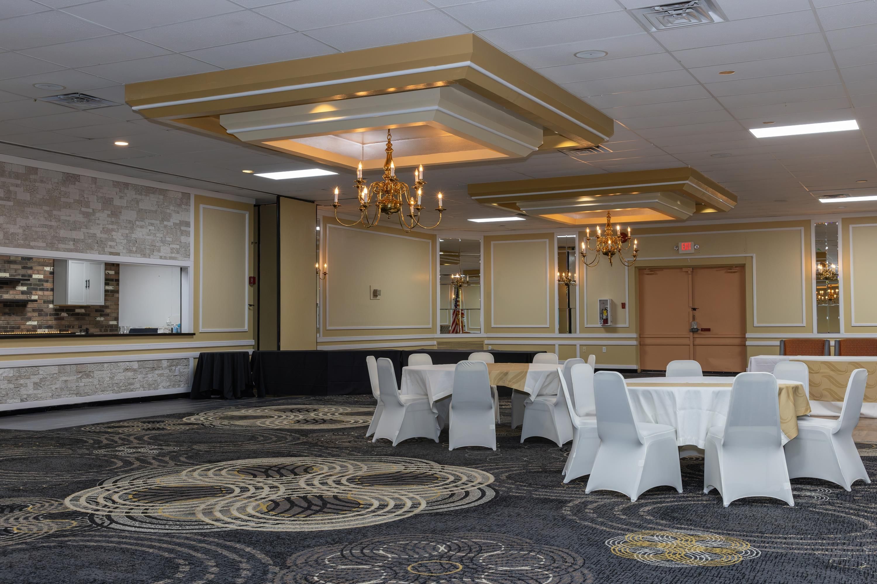 A conference room with white chairs, a round table, chandeliers, and a patterned carpet.
