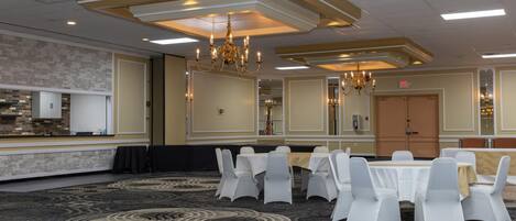 A conference room with white chairs, a round table, chandeliers, and a patterned carpet.