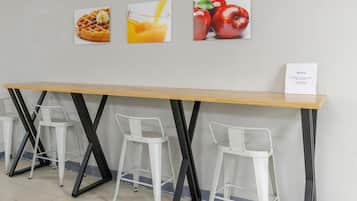 Una barra de desayuno con tres sillas blancas, una mesa de madera y tres cuadros en la pared.