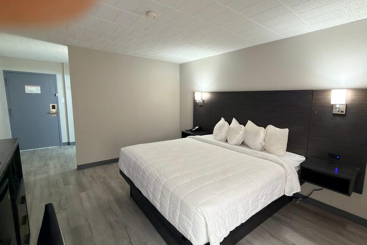 A hotel room with a large bed, a bedside table, a nightstand, a wall-mounted light, and a door.