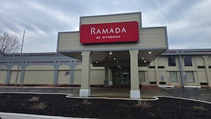 Rakennuksessa on kyltti, jossa lukee ”RAMADA BY WYNDHAM”, ja sen sisäänkäynti on katettu.