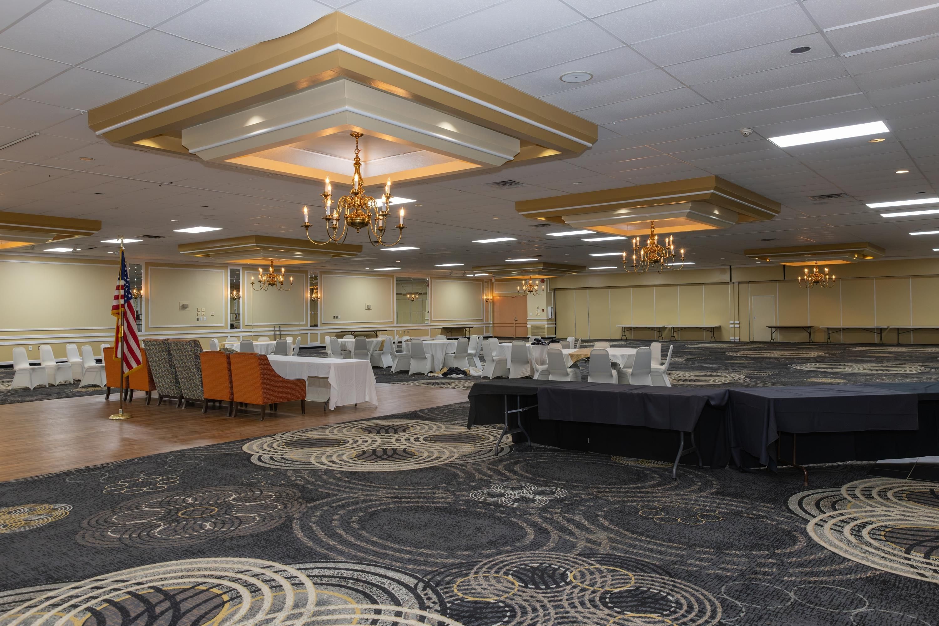 A banquet hall with tables set for events, chandeliers, and an American flag.