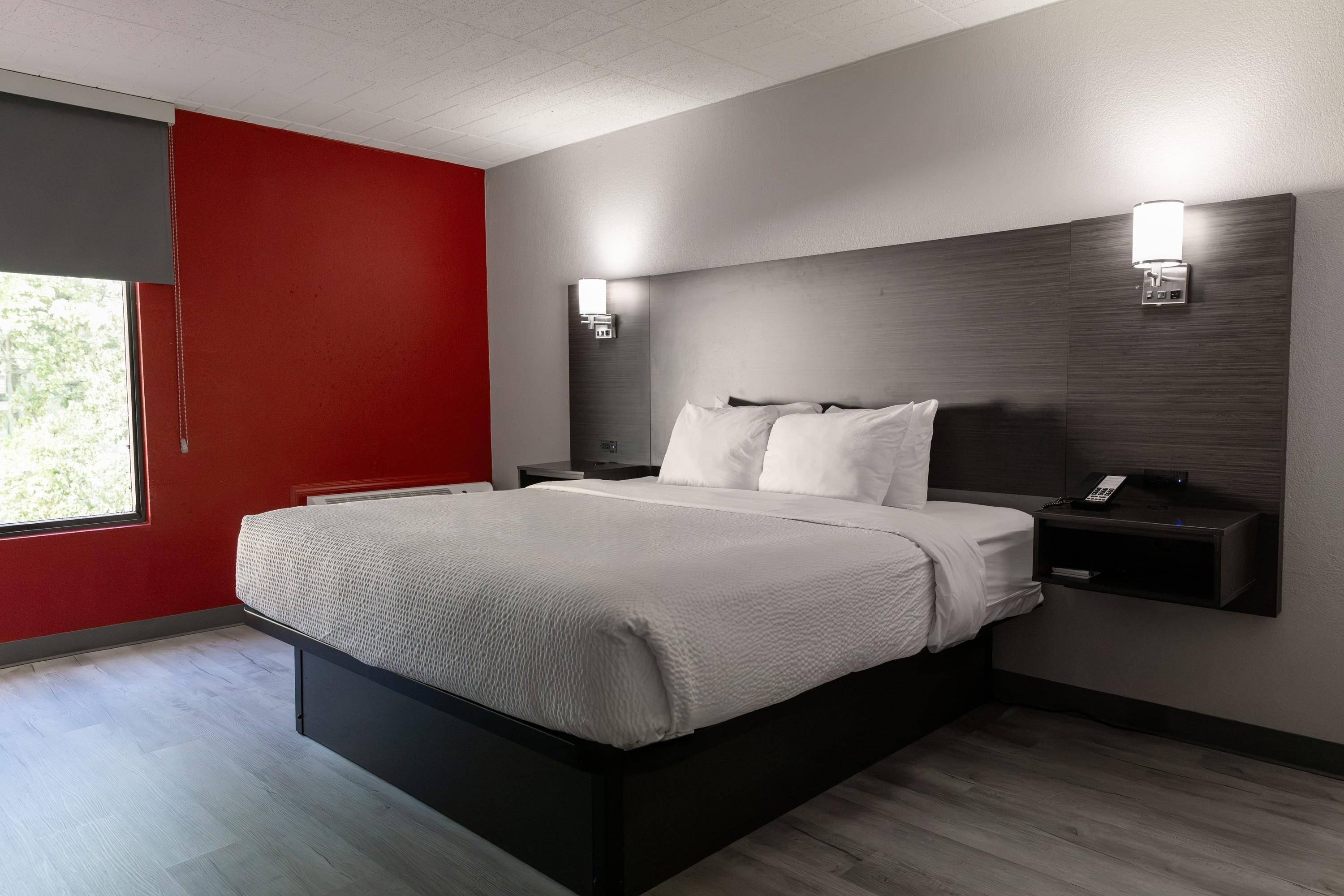 Een moderne hotelkamer met een groot bed, een nachtkastje, een wandlamp en een raam met uitzicht op bomen.