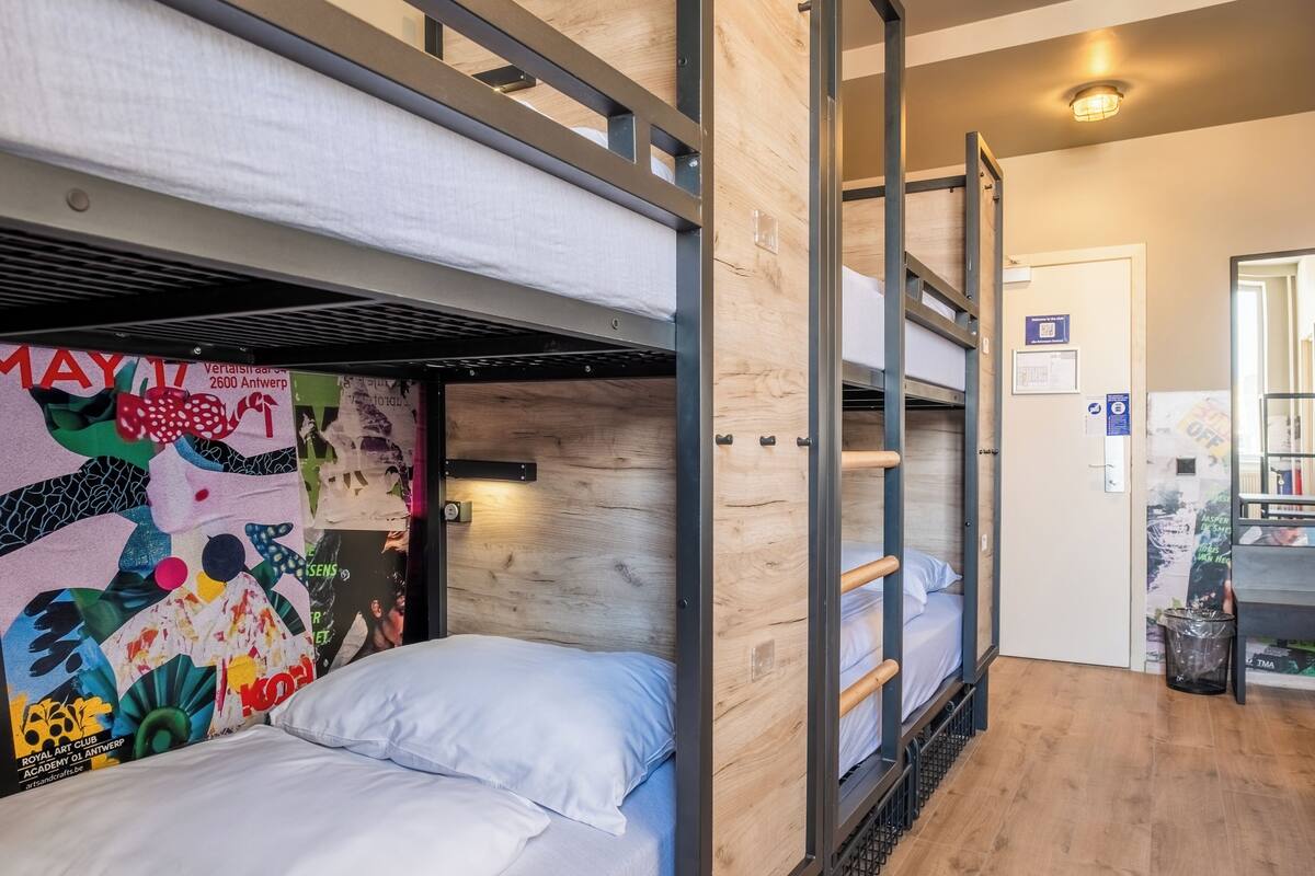 A bunk bed room with a wooden wall and a colorful mural. There is a door with a sign and a trash can.