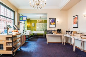 A hotel lobby with a reception desk, a chandelier, framed artwork, and a coffee station. - a&o Antwerpen Centraal (Antwerp)